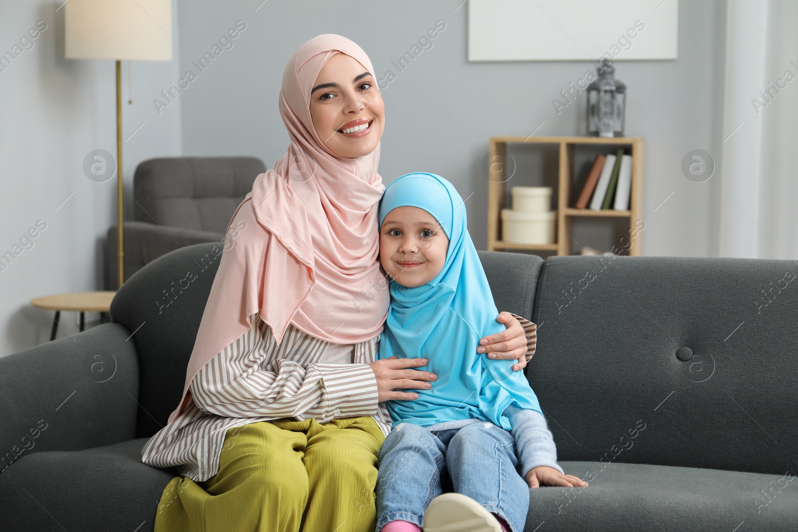 Photo of Muslim mother and her daughter sitting on sofa at home