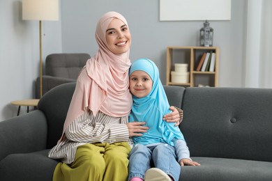 Photo of Muslim mother and her daughter sitting on sofa at home