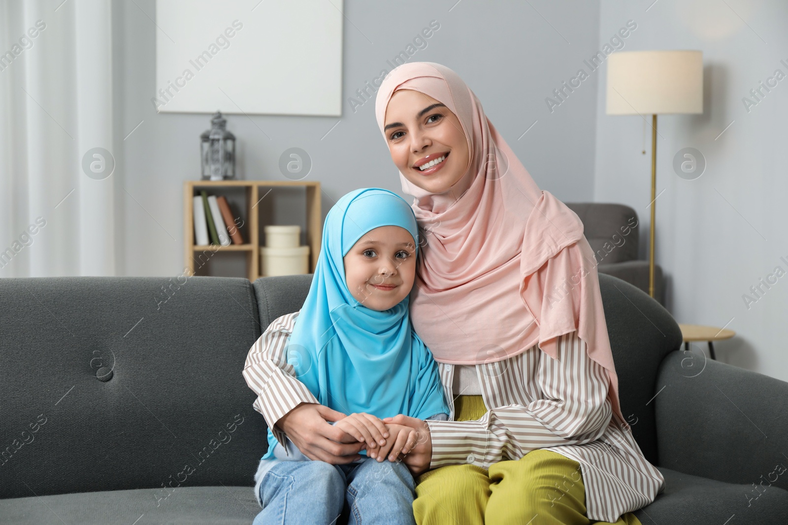 Photo of Muslim mother and her daughter sitting on sofa at home