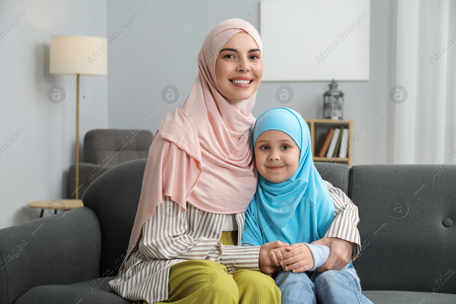 Photo of Muslim mother and her daughter sitting on sofa at home