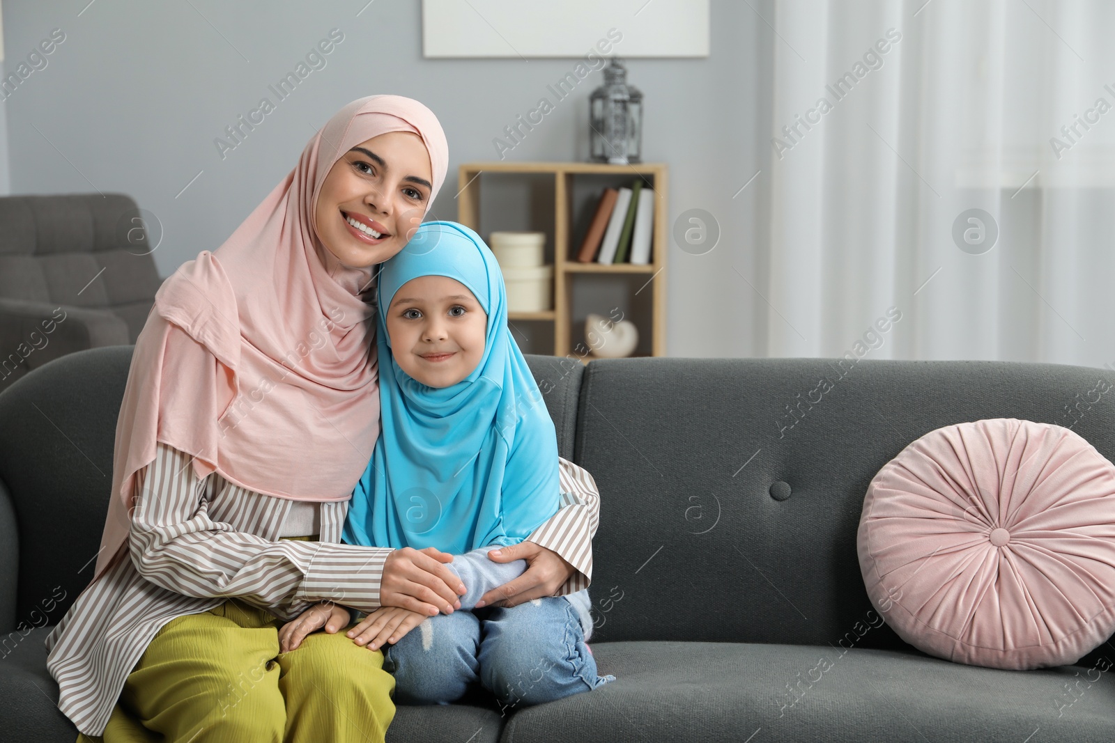 Photo of Muslim mother and her daughter sitting on sofa at home, space for text