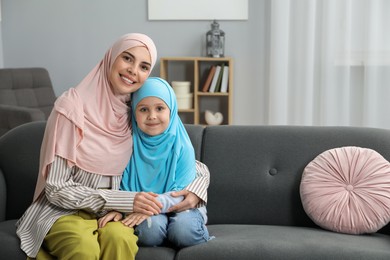 Photo of Muslim mother and her daughter sitting on sofa at home, space for text