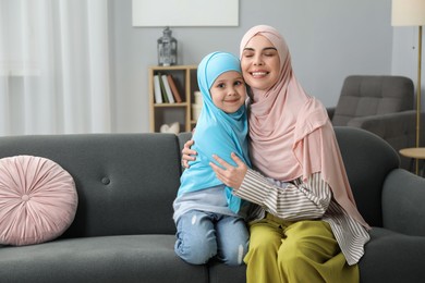 Photo of Muslim mother and her daughter sitting on sofa at home, space for text