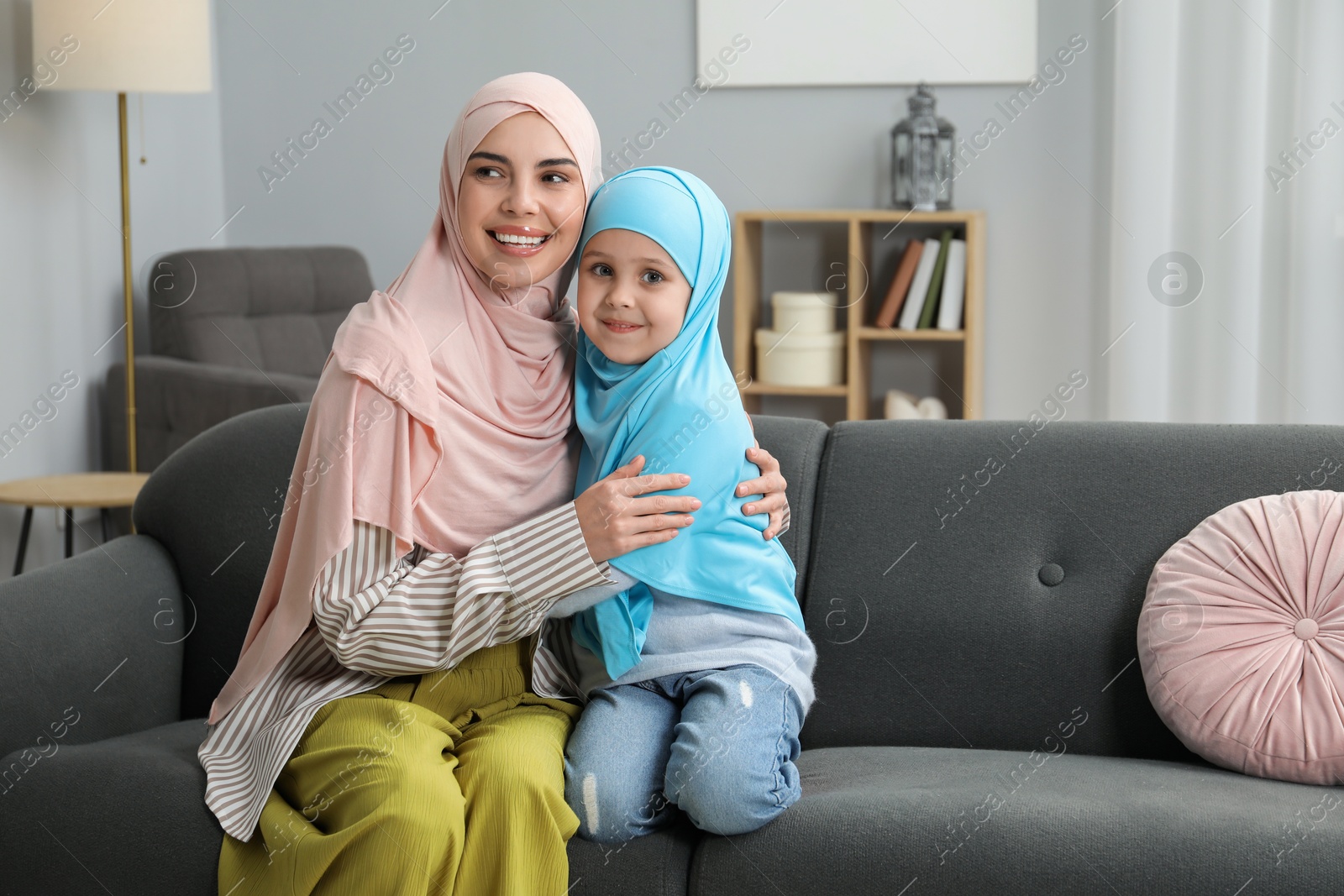 Photo of Muslim mother and her daughter sitting on sofa at home, space for text