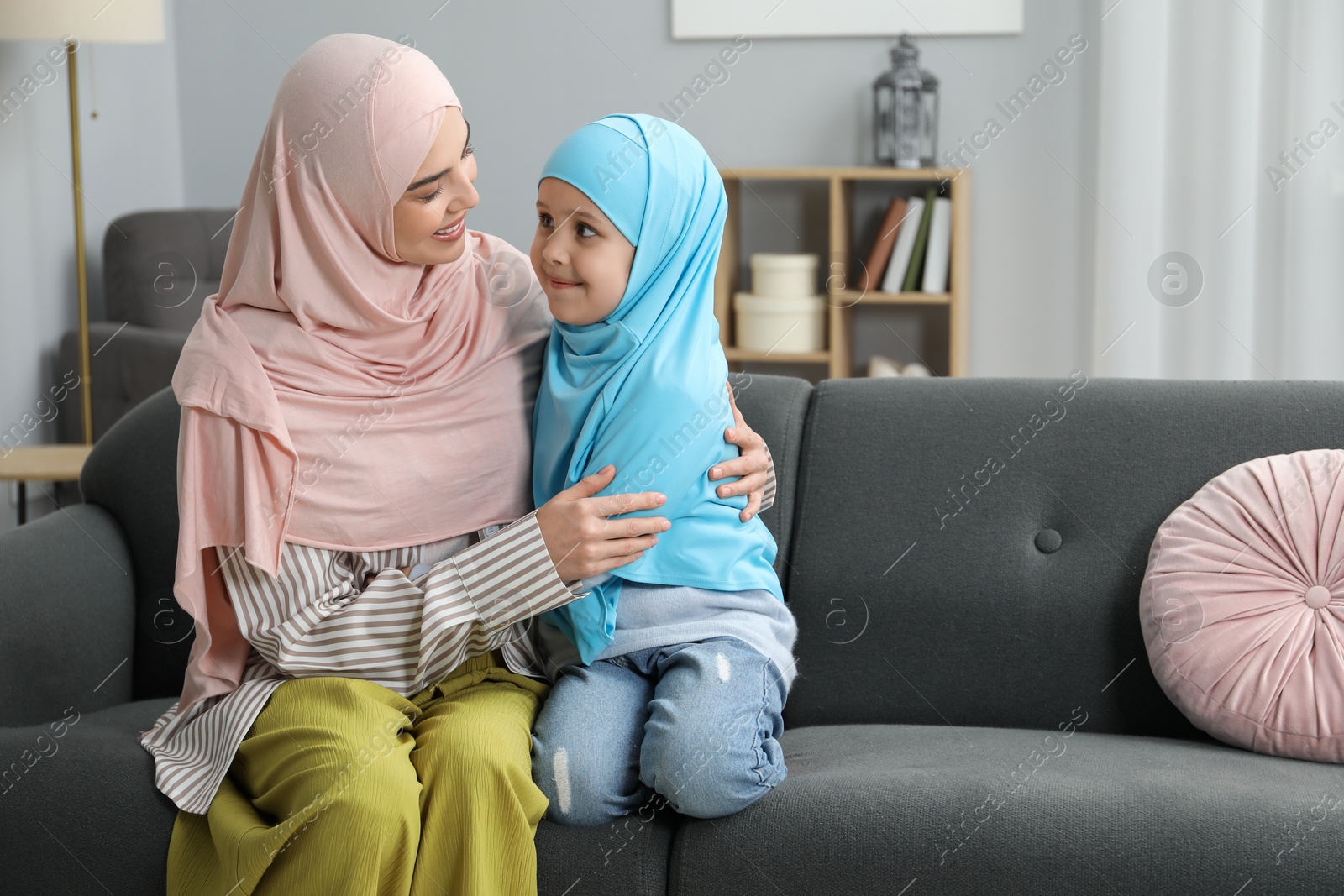 Photo of Muslim mother and her daughter sitting on sofa at home, space for text