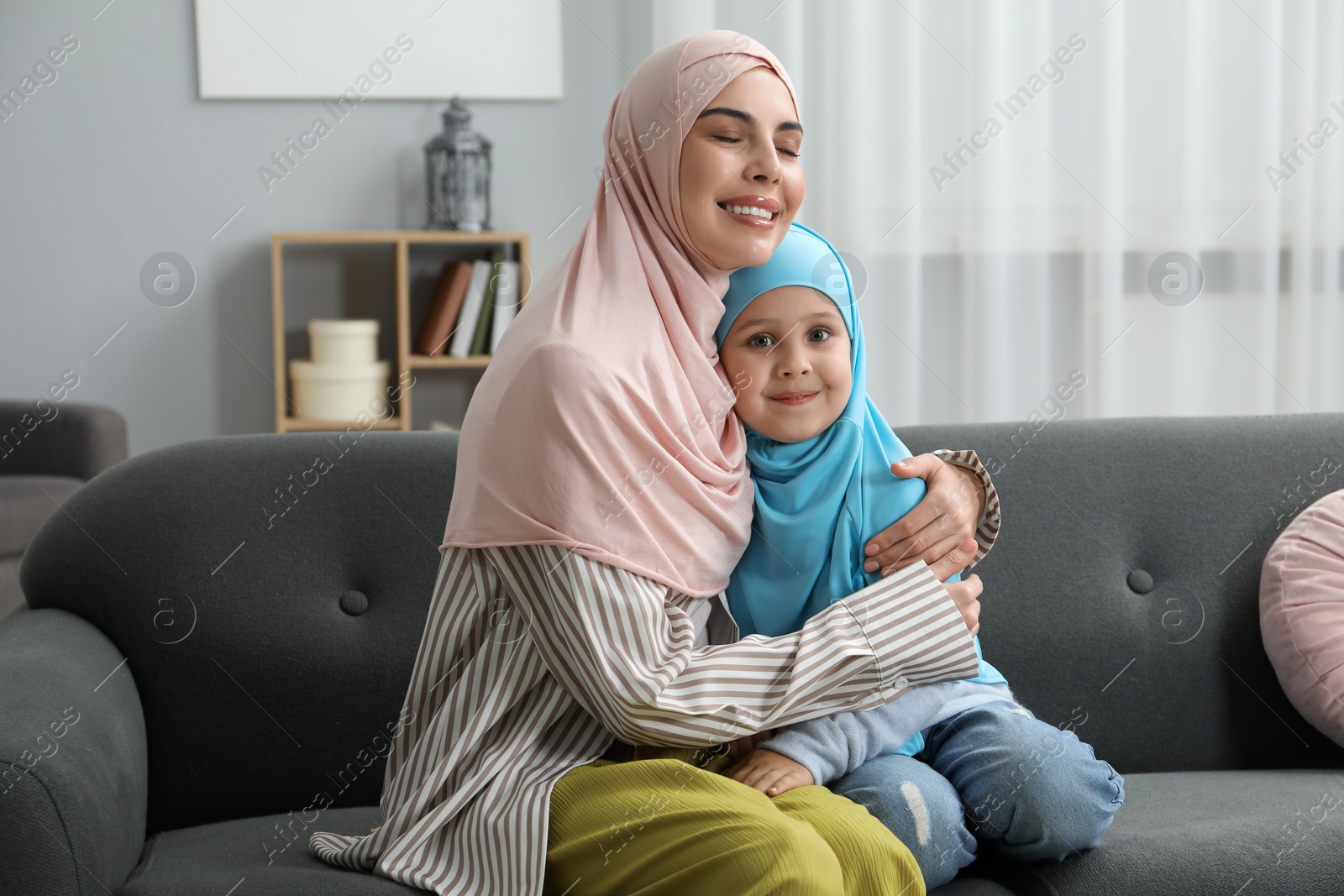 Photo of Muslim mother and her daughter sitting on sofa at home