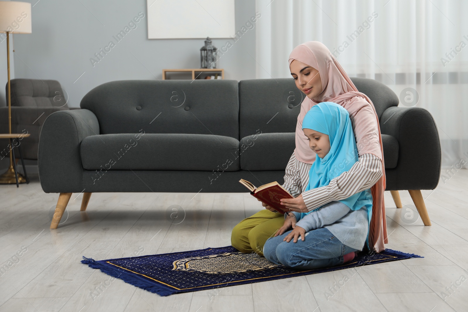 Photo of Muslim woman and her daughter with Quran praying on mat at home