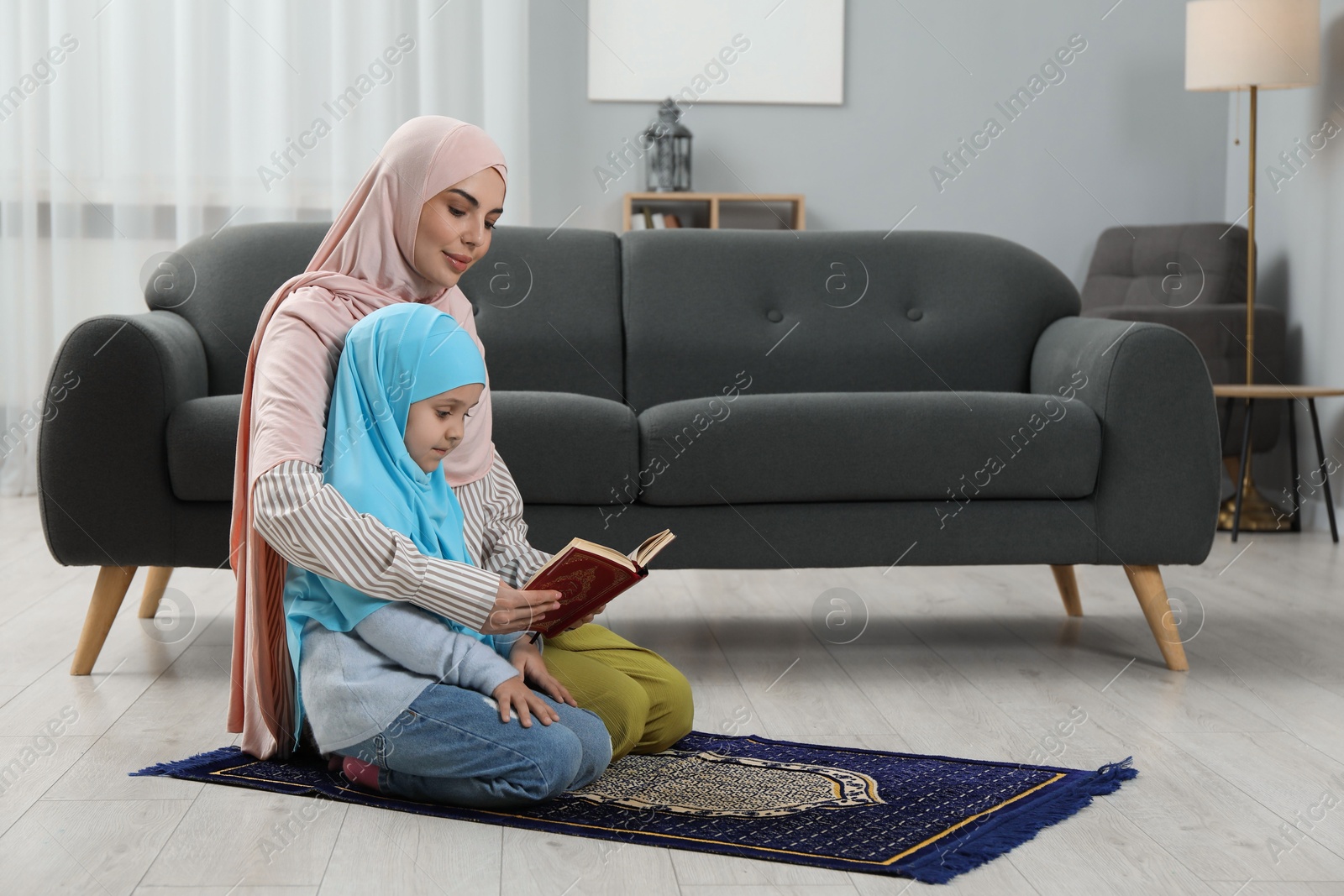 Photo of Muslim woman and her daughter with Quran praying on mat at home