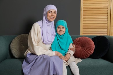 Photo of Muslim woman and her daughter sitting on sofa at home