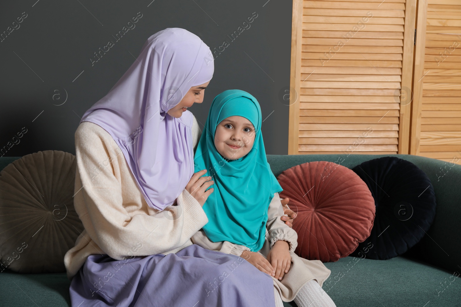 Photo of Muslim woman and her daughter sitting on sofa at home