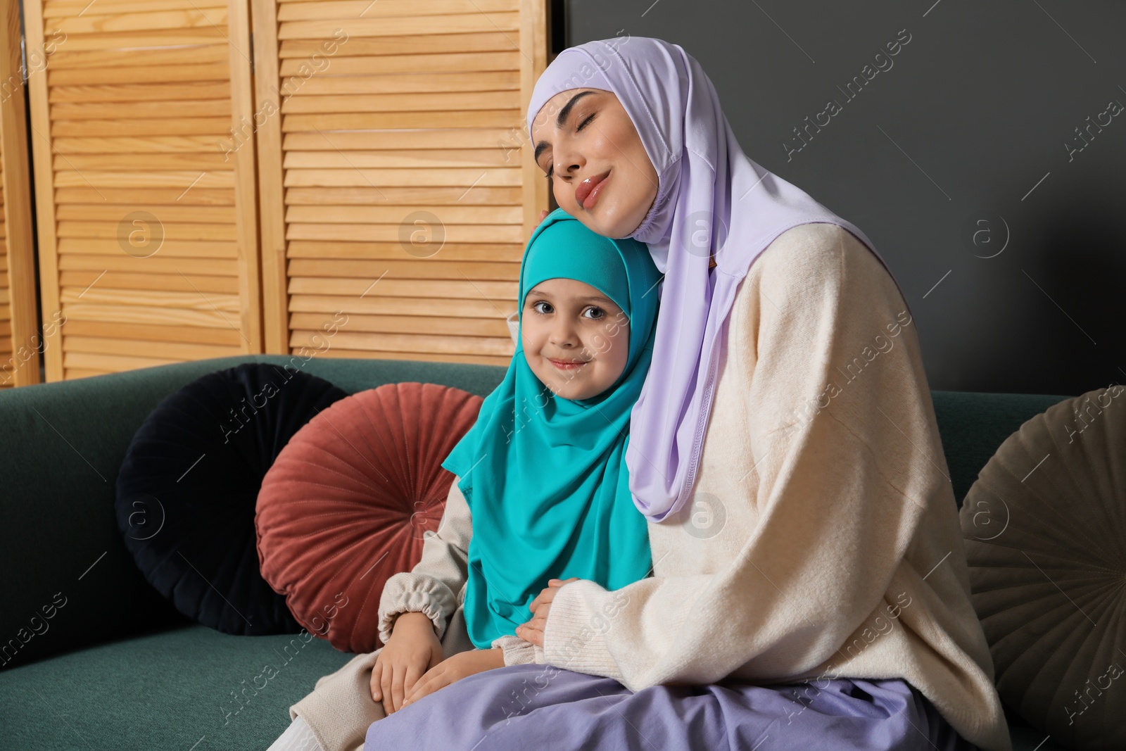 Photo of Muslim woman and her daughter sitting on sofa at home