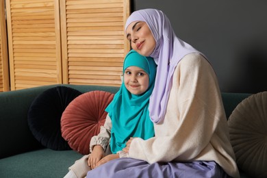 Muslim woman and her daughter sitting on sofa at home