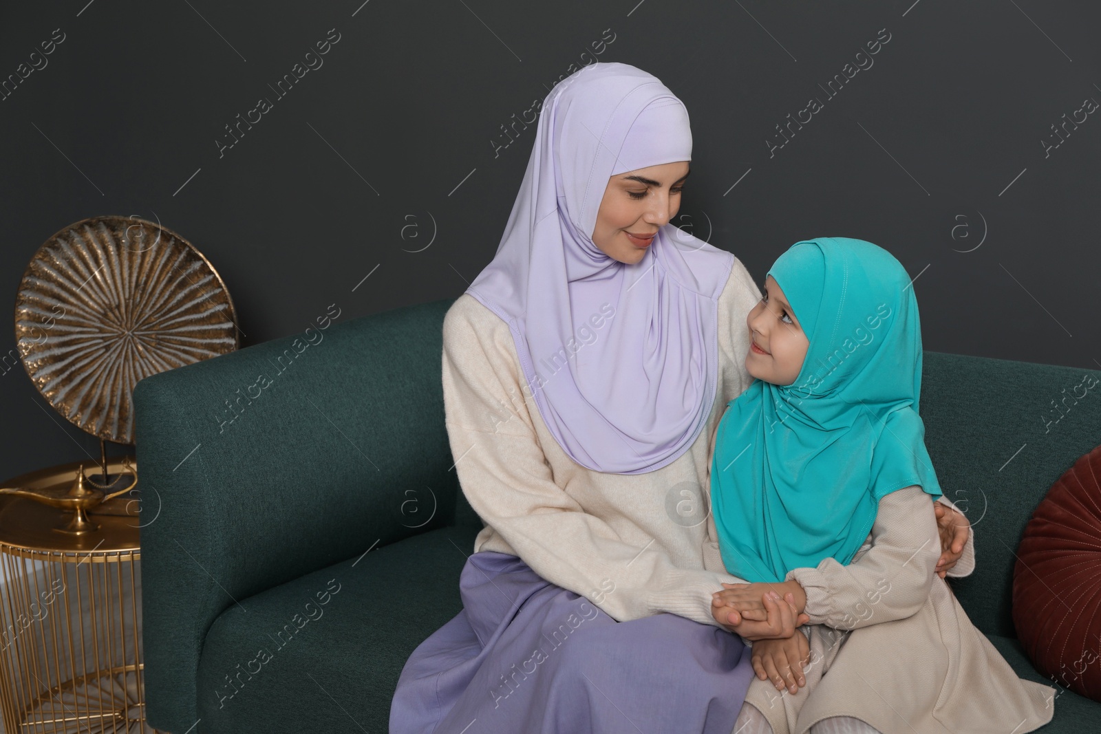 Photo of Muslim woman and her daughter sitting on sofa at home