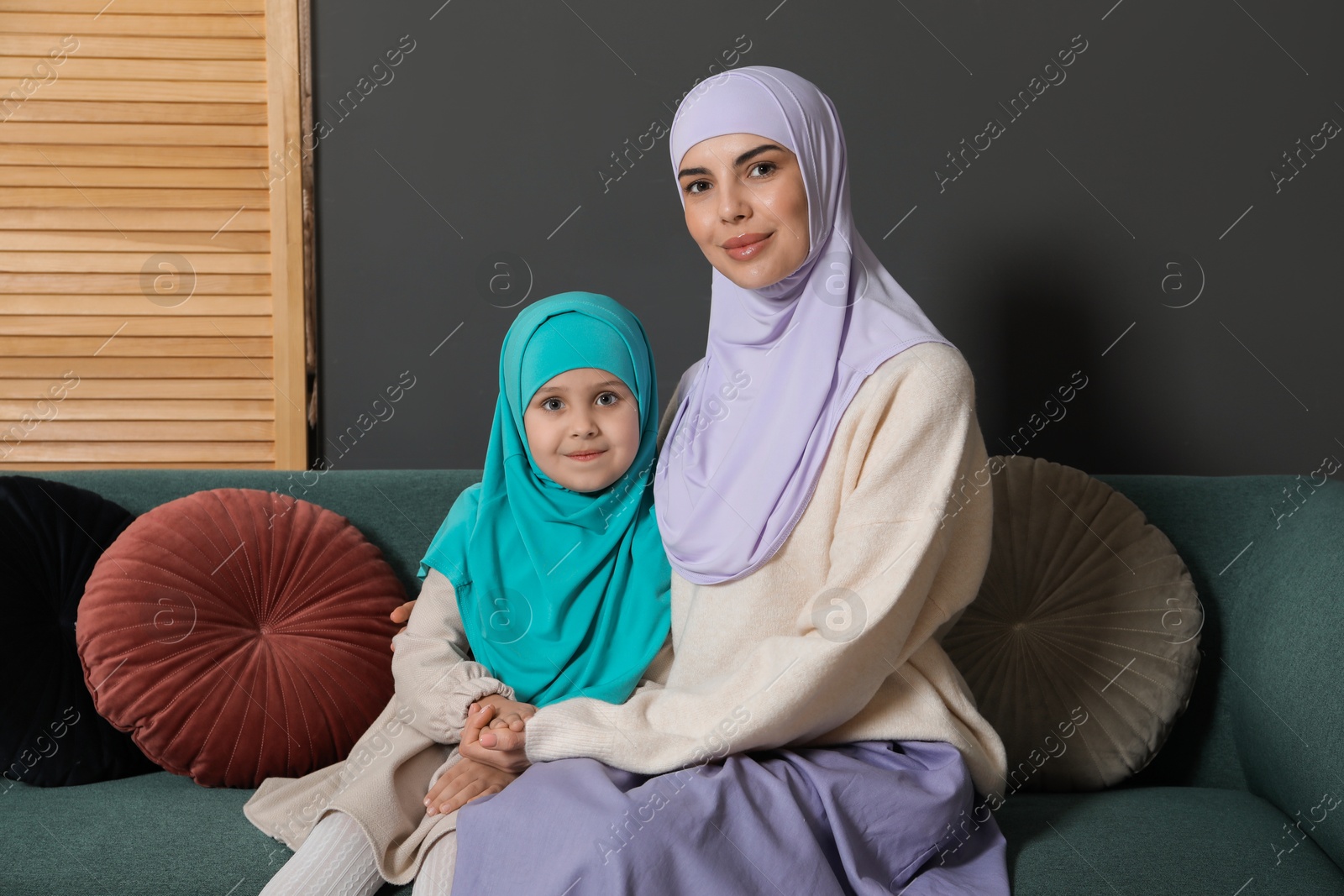 Photo of Muslim woman and her daughter sitting on sofa at home