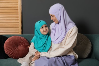 Photo of Muslim woman and her daughter sitting on sofa at home