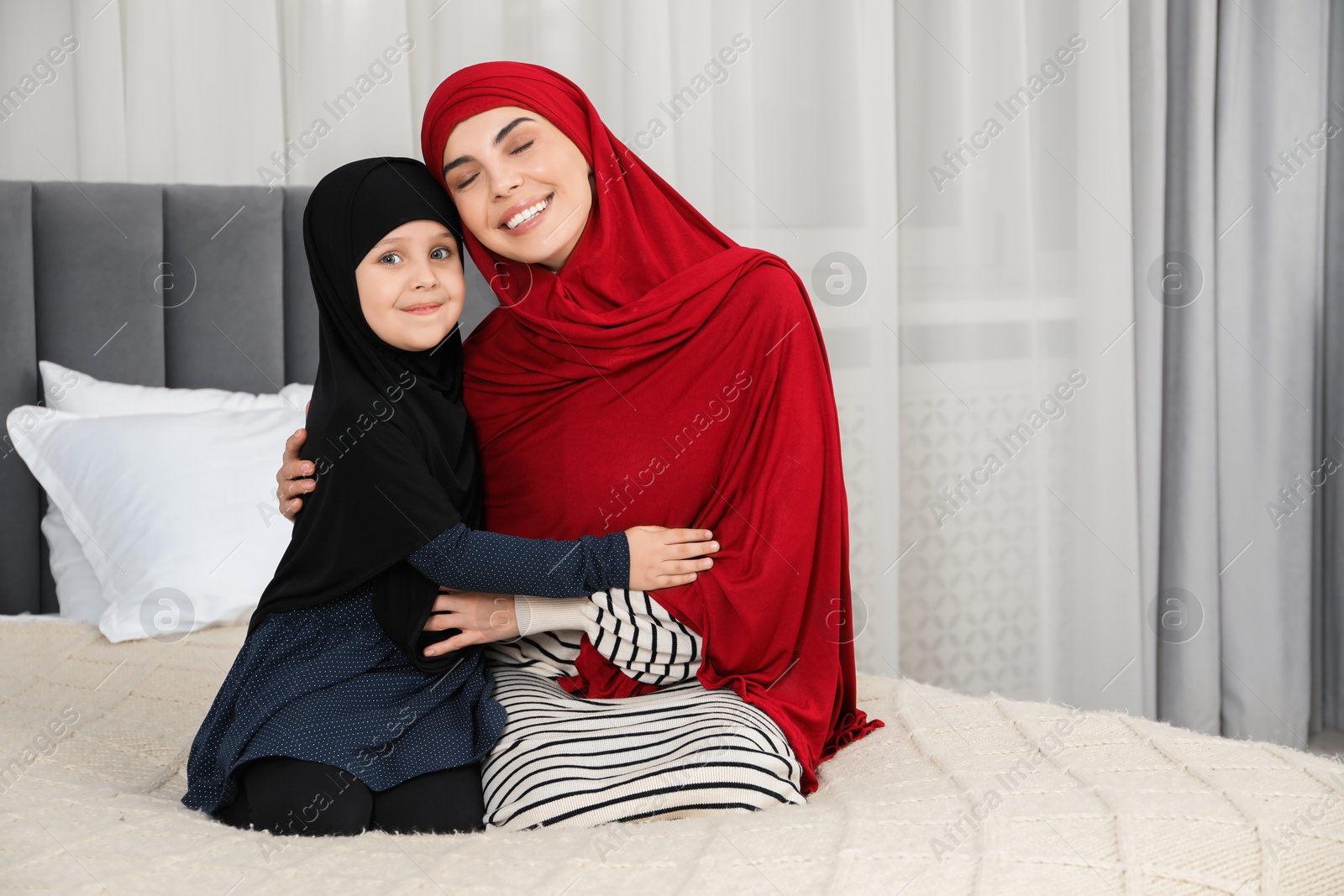 Photo of Muslim woman and her daughter spending time together at home, space for text