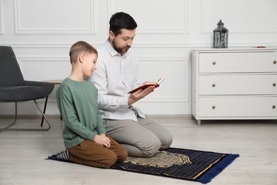 Photo of Muslim man and his son with Quran praying on mat at home