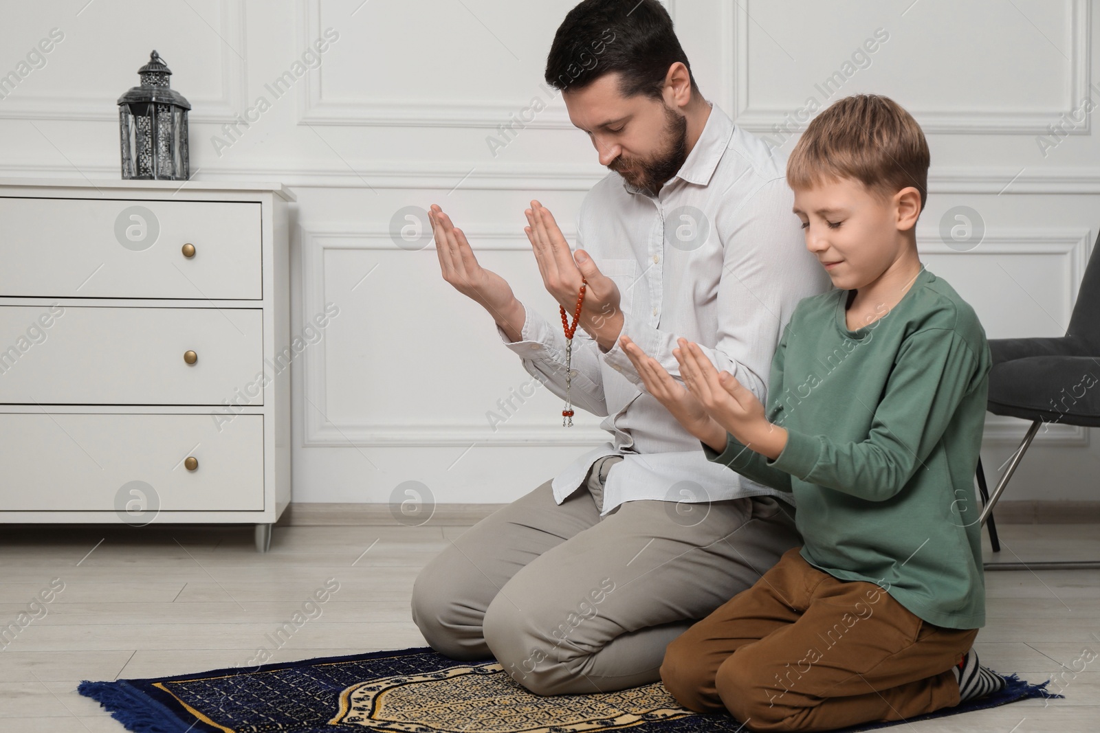 Photo of Muslim man and his son with beads praying on mat at home