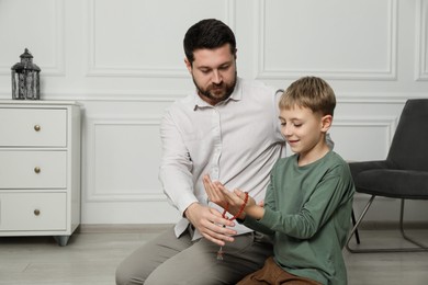 Photo of Muslim man and his son with beads praying on mat at home