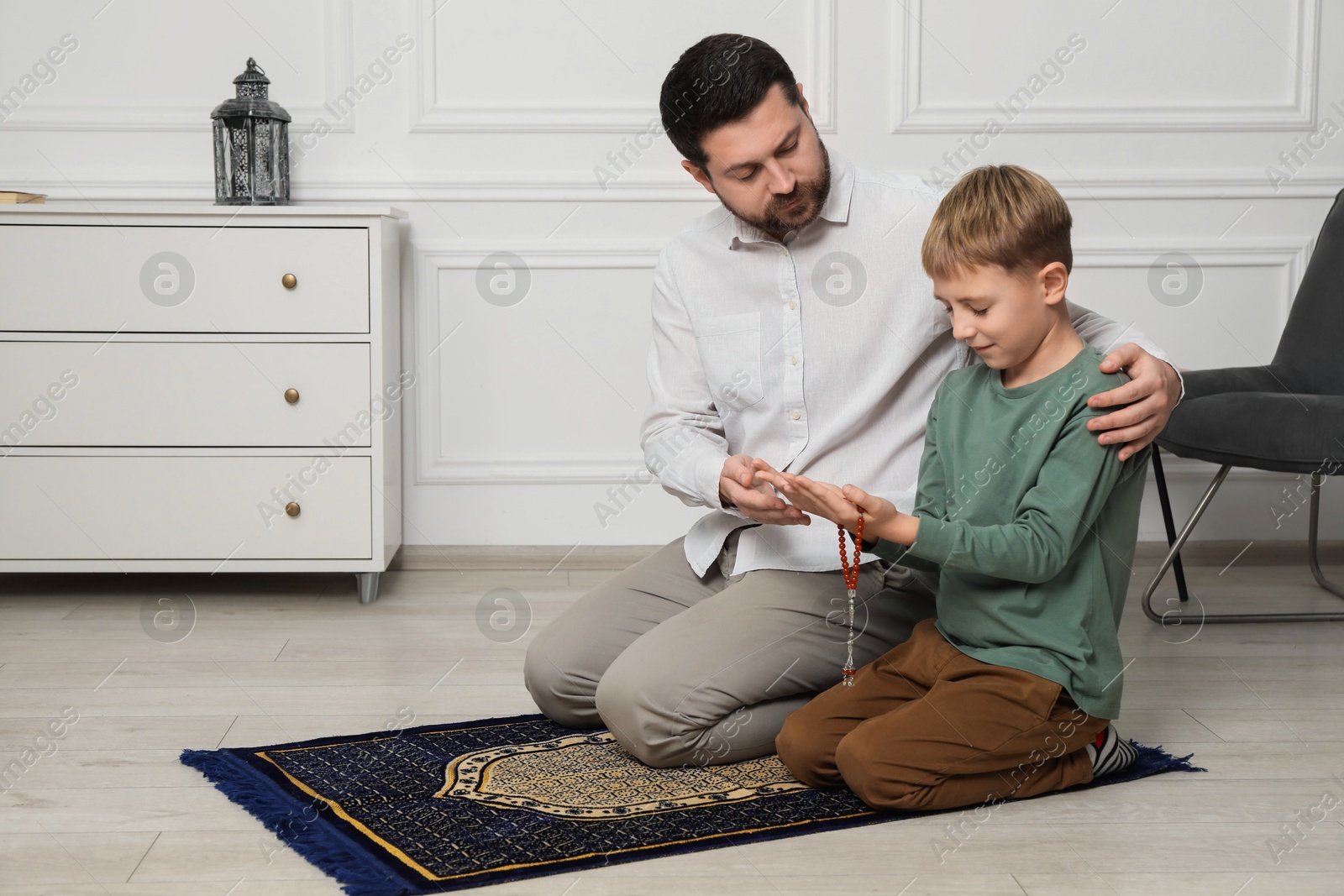 Photo of Muslim man and his son with beads praying on mat at home