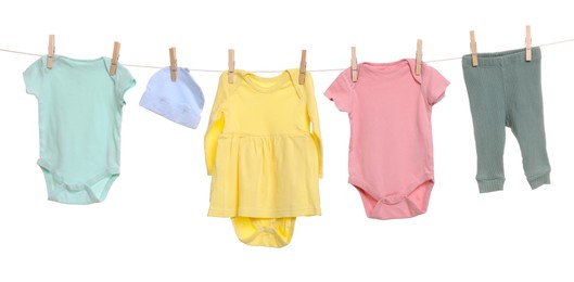 Different baby clothes drying on laundry line against white background