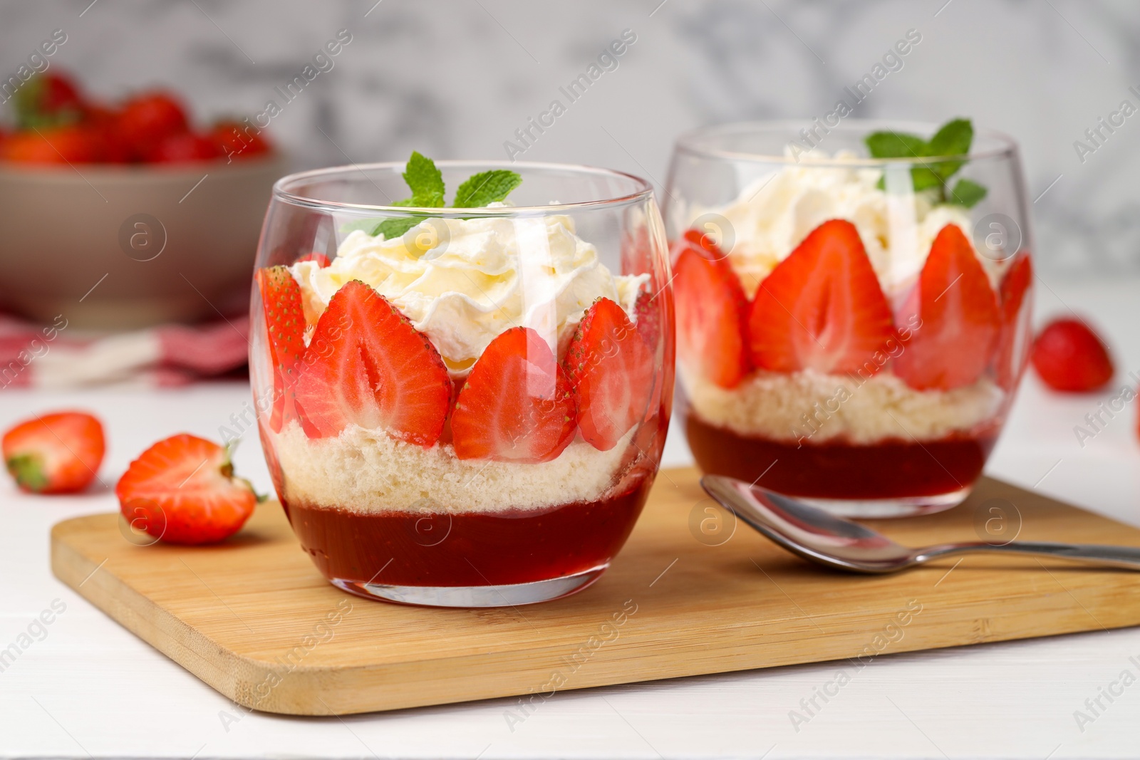 Photo of Tasty trifle dessert. Sponge cake, strawberries, jam and whipped cream in glasses on white table, closeup