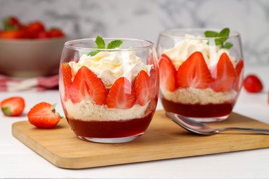 Photo of Tasty trifle dessert. Sponge cake, strawberries, jam and whipped cream in glasses on white table, closeup