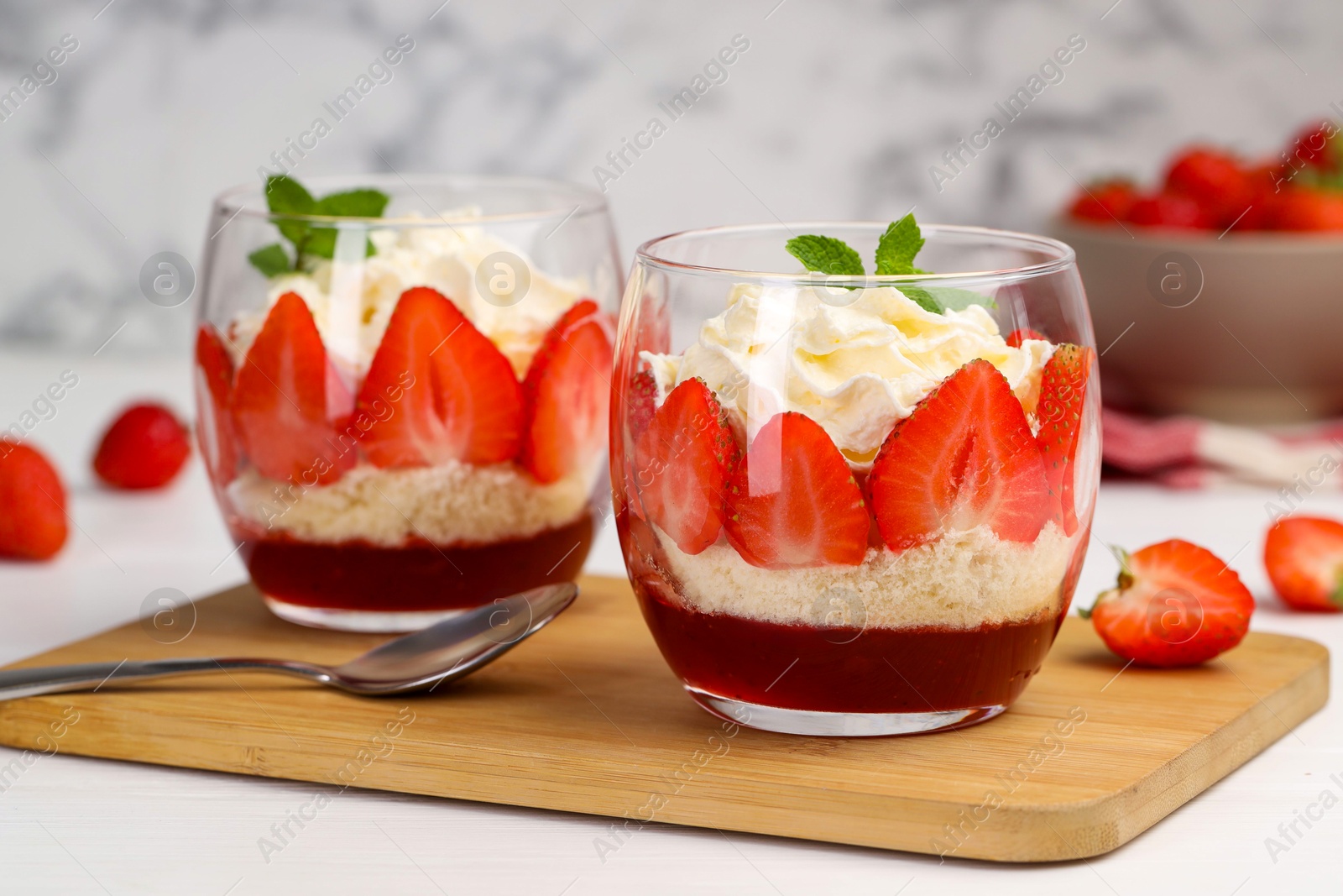 Photo of Tasty trifle dessert. Sponge cake, strawberries, jam and whipped cream in glasses on white table, closeup