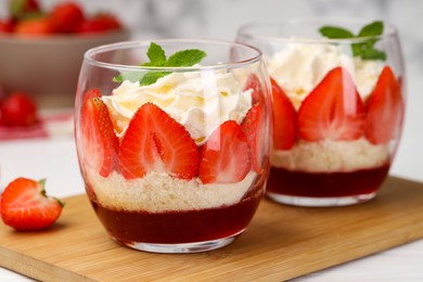 Photo of Tasty trifle dessert. Sponge cake, strawberries, jam and whipped cream in glasses on table, closeup