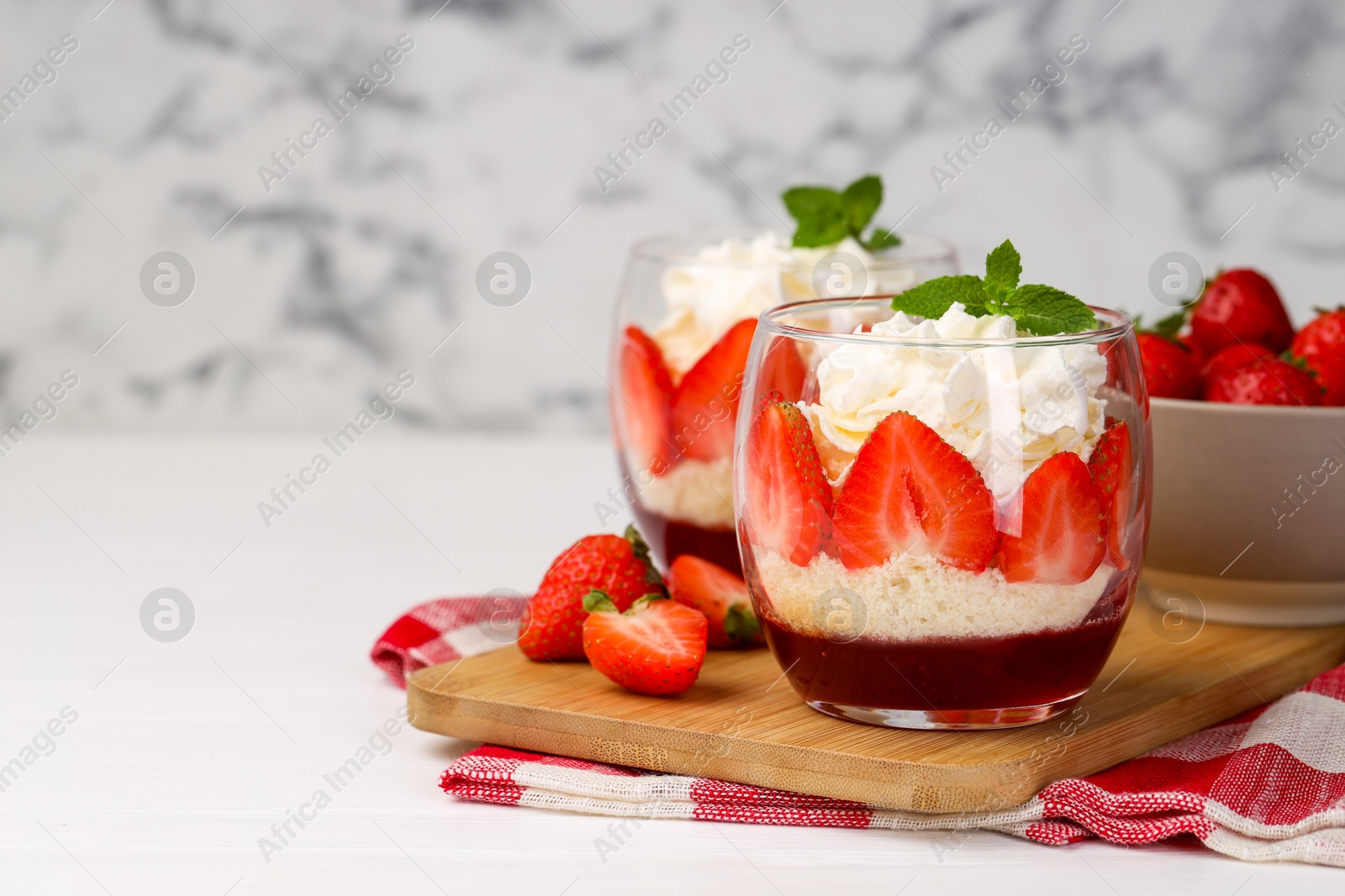 Photo of Tasty trifle dessert. Sponge cake, strawberries, jam and whipped cream in glasses on white table