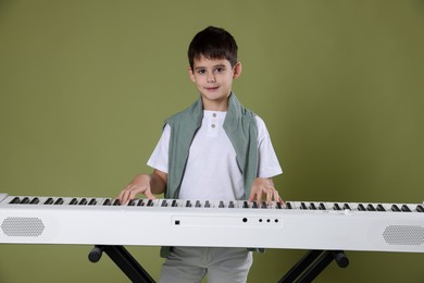 Photo of Cute boy playing synthesizer on olive background