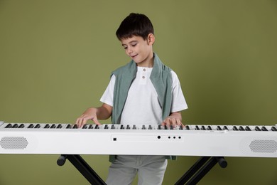 Photo of Cute boy playing synthesizer on olive background