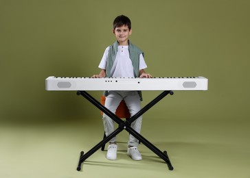 Photo of Cute boy playing synthesizer on olive background