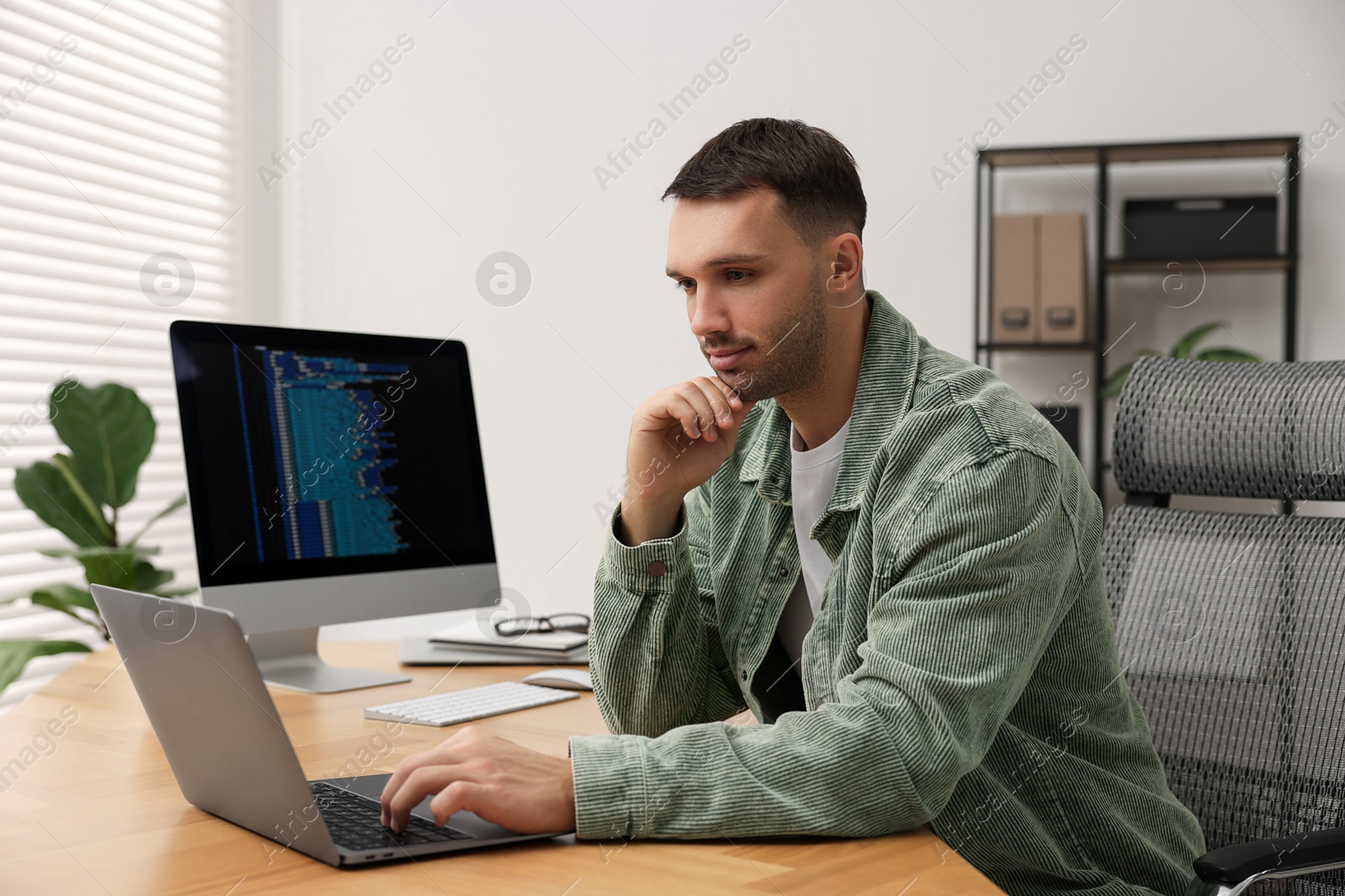 Photo of Programmer working on laptop at wooden desk indoors