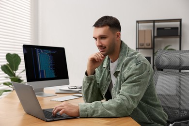 Photo of Programmer working on laptop at wooden desk indoors