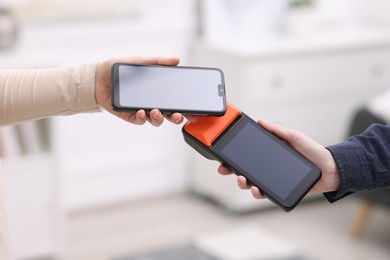 Photo of Woman paying with smartphone via terminal against blurred background, closeup