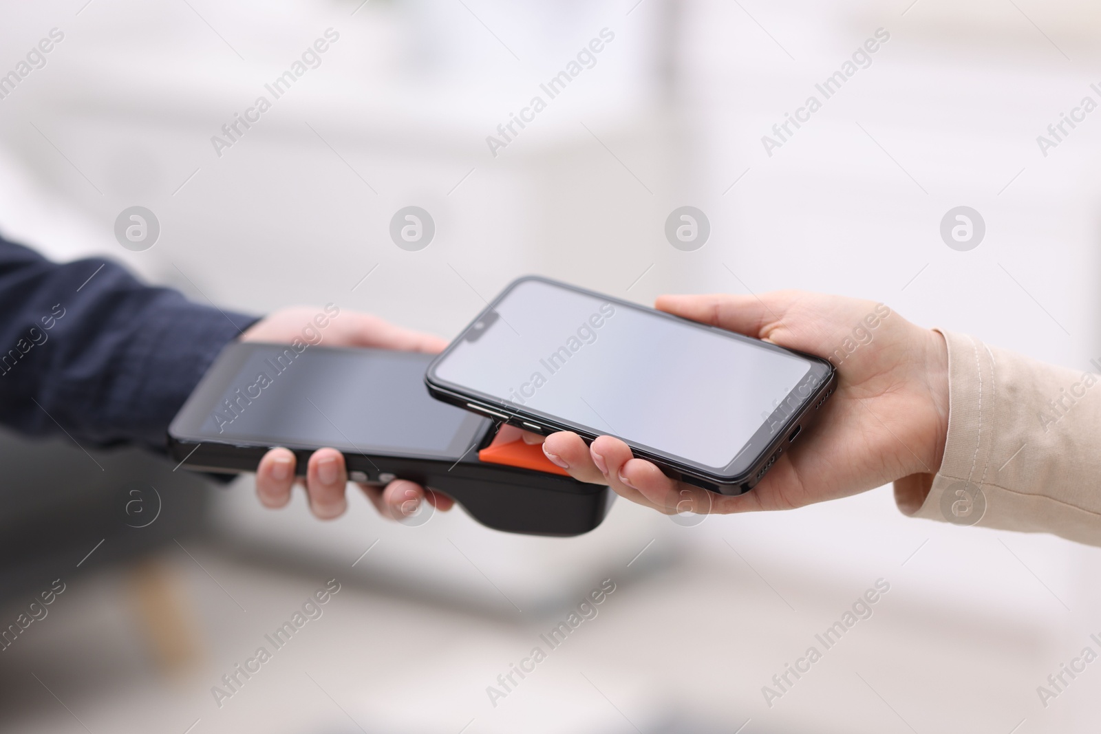 Photo of Woman paying with smartphone via terminal against blurred background, closeup