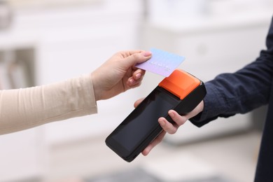 Photo of Woman paying with credit card via terminal against blurred background, closeup