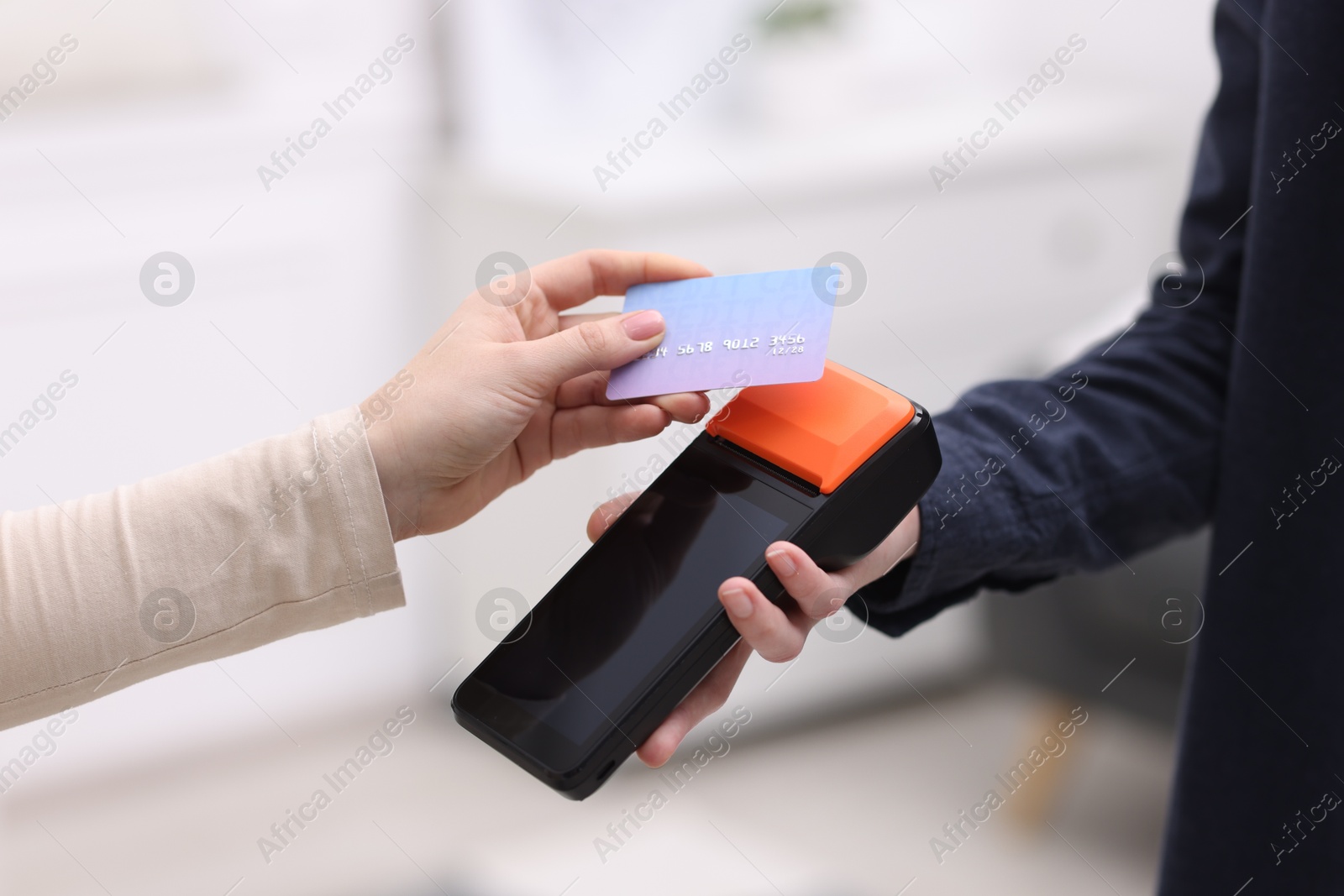 Photo of Woman paying with credit card via terminal against blurred background, closeup