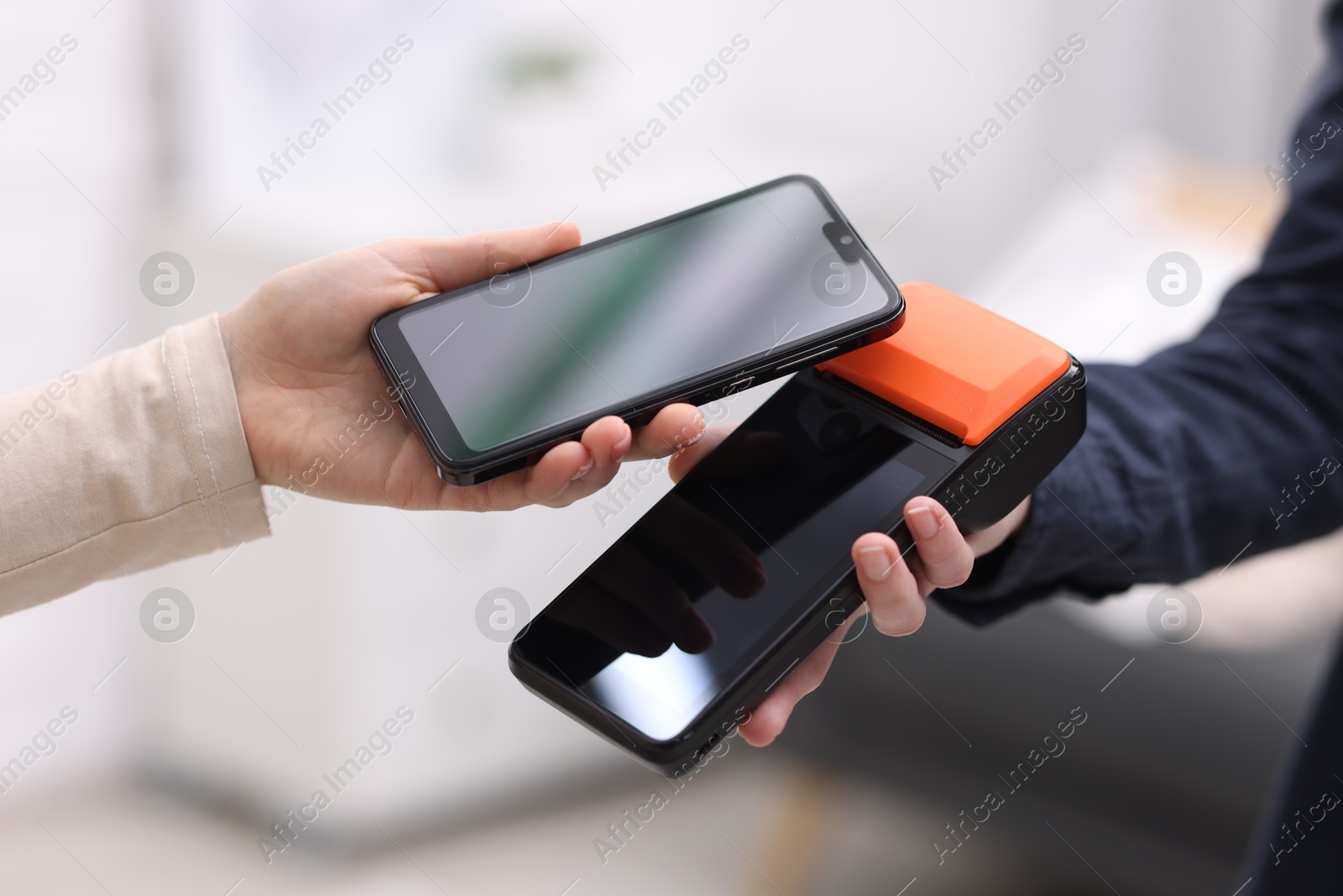 Photo of Woman paying with smartphone via terminal against blurred background, closeup