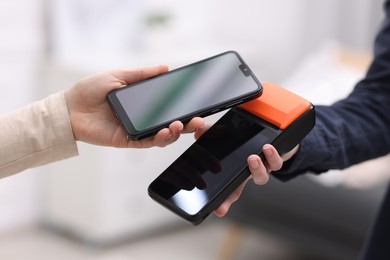 Photo of Woman paying with smartphone via terminal against blurred background, closeup