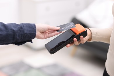 Photo of Woman paying with credit card via terminal against blurred background, closeup