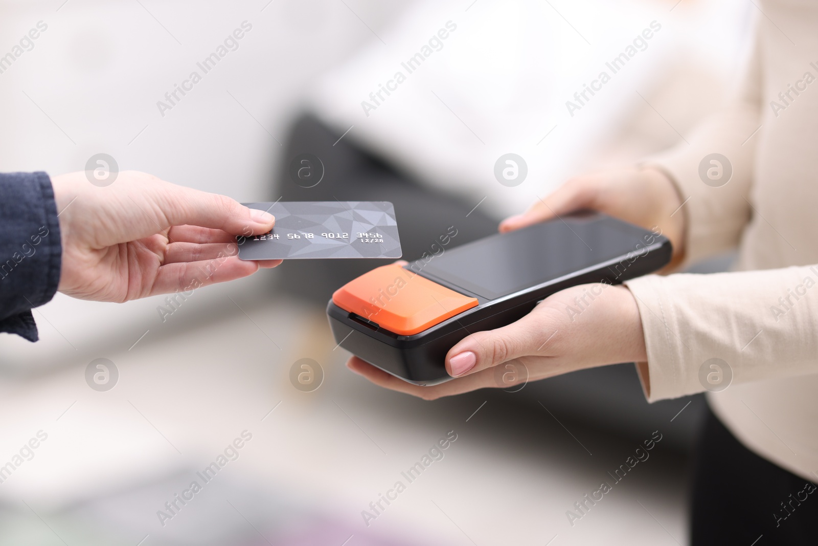 Photo of Woman paying with credit card via terminal against blurred background, closeup