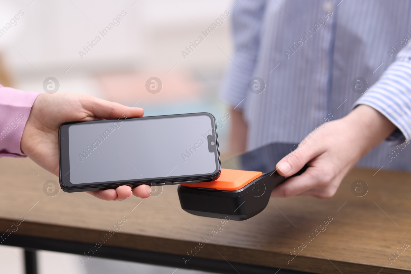 Photo of Woman paying with smartphone via terminal at wooden counter indoors, closeup