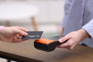 Photo of Woman paying with credit card via terminal at wooden counter indoors, closeup