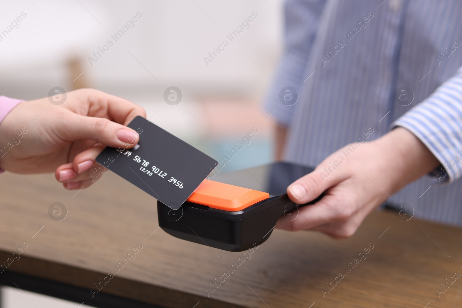 Photo of Woman paying with credit card via terminal at wooden counter indoors, closeup