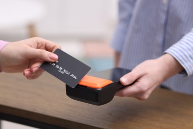 Woman paying with credit card via terminal at wooden counter indoors, closeup