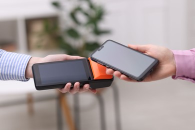 Photo of Woman paying with smartphone via terminal against blurred background, closeup