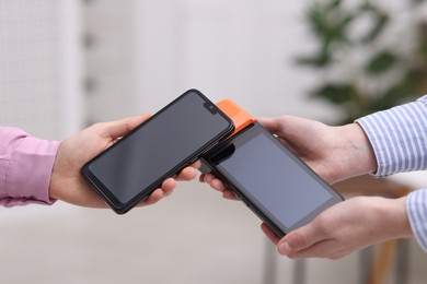 Photo of Woman paying with smartphone via terminal against blurred background, closeup