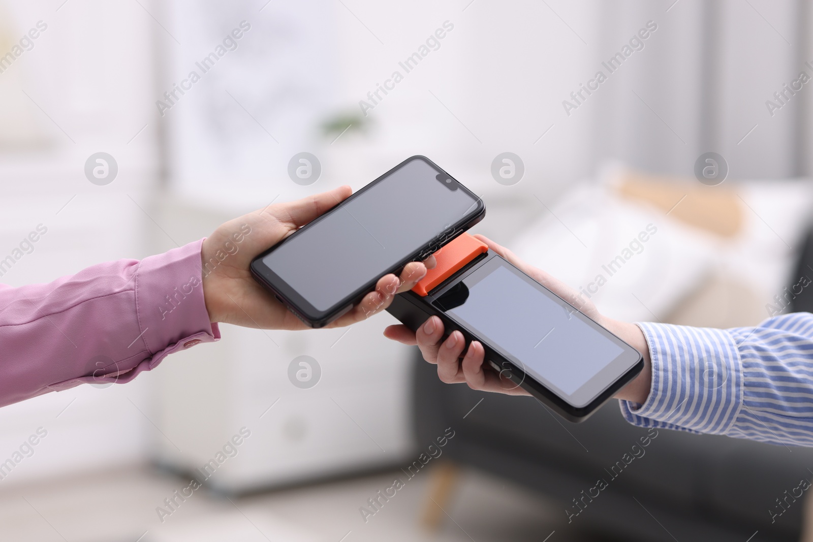 Photo of Woman paying with smartphone via terminal against blurred background, closeup